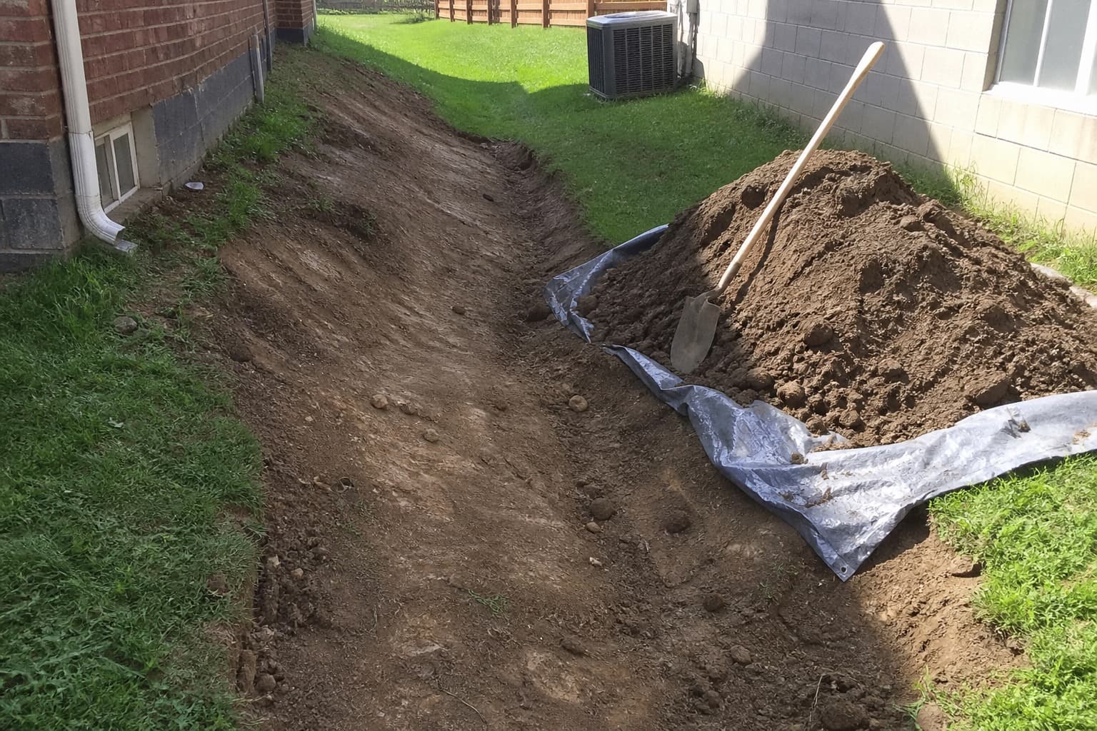 Yard grading work with soil beside a shallow swale for surface drainage