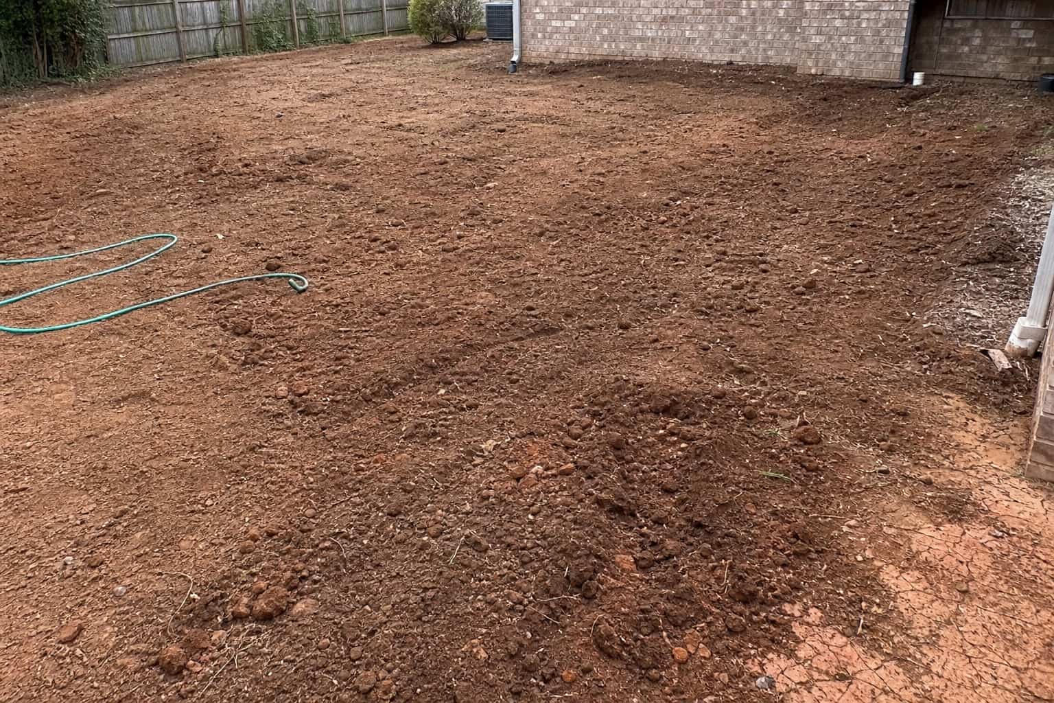Bare soil lawn area before sod with hose and uneven grade visible