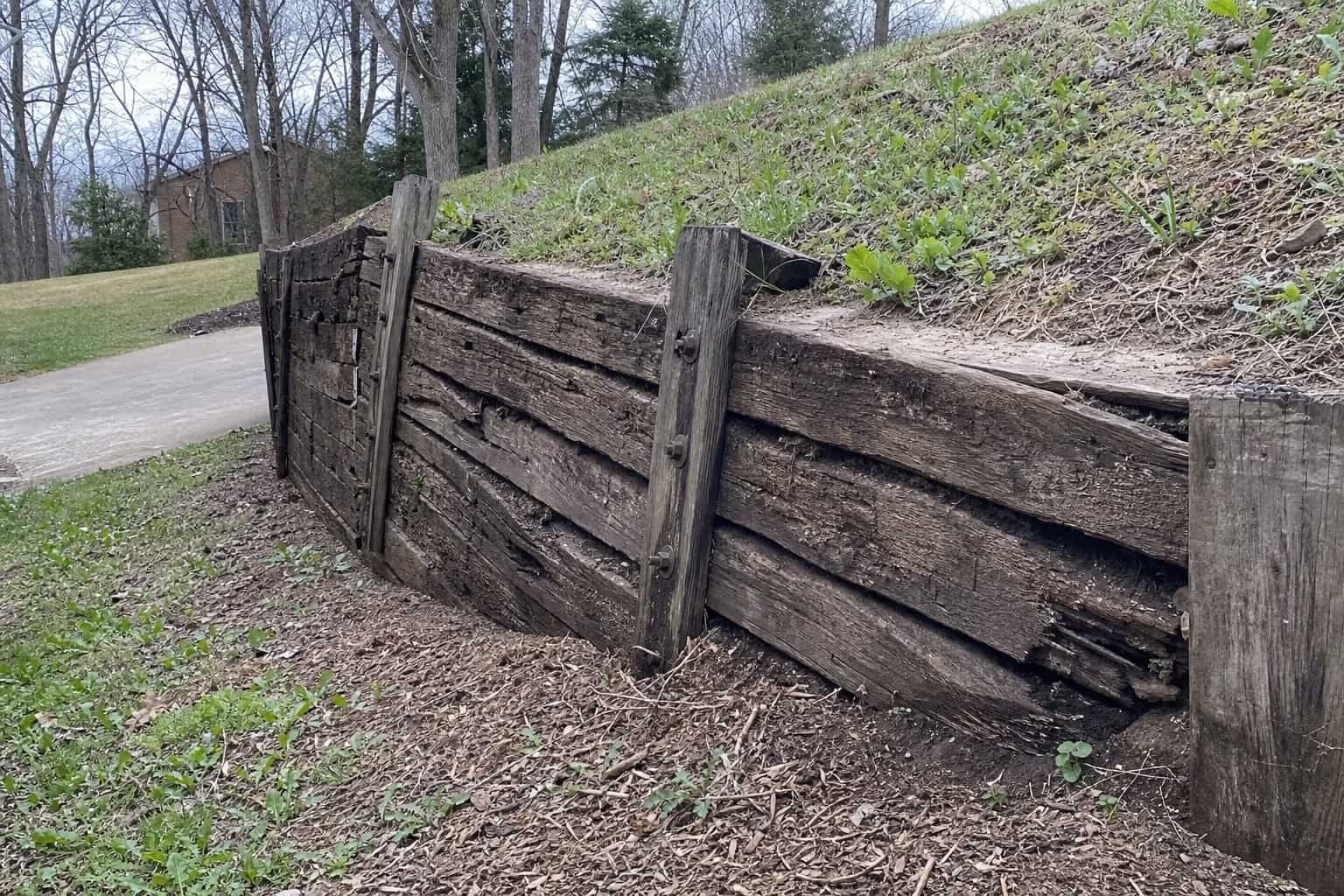Aging timber tie retaining wall leaning and bowing on a slope