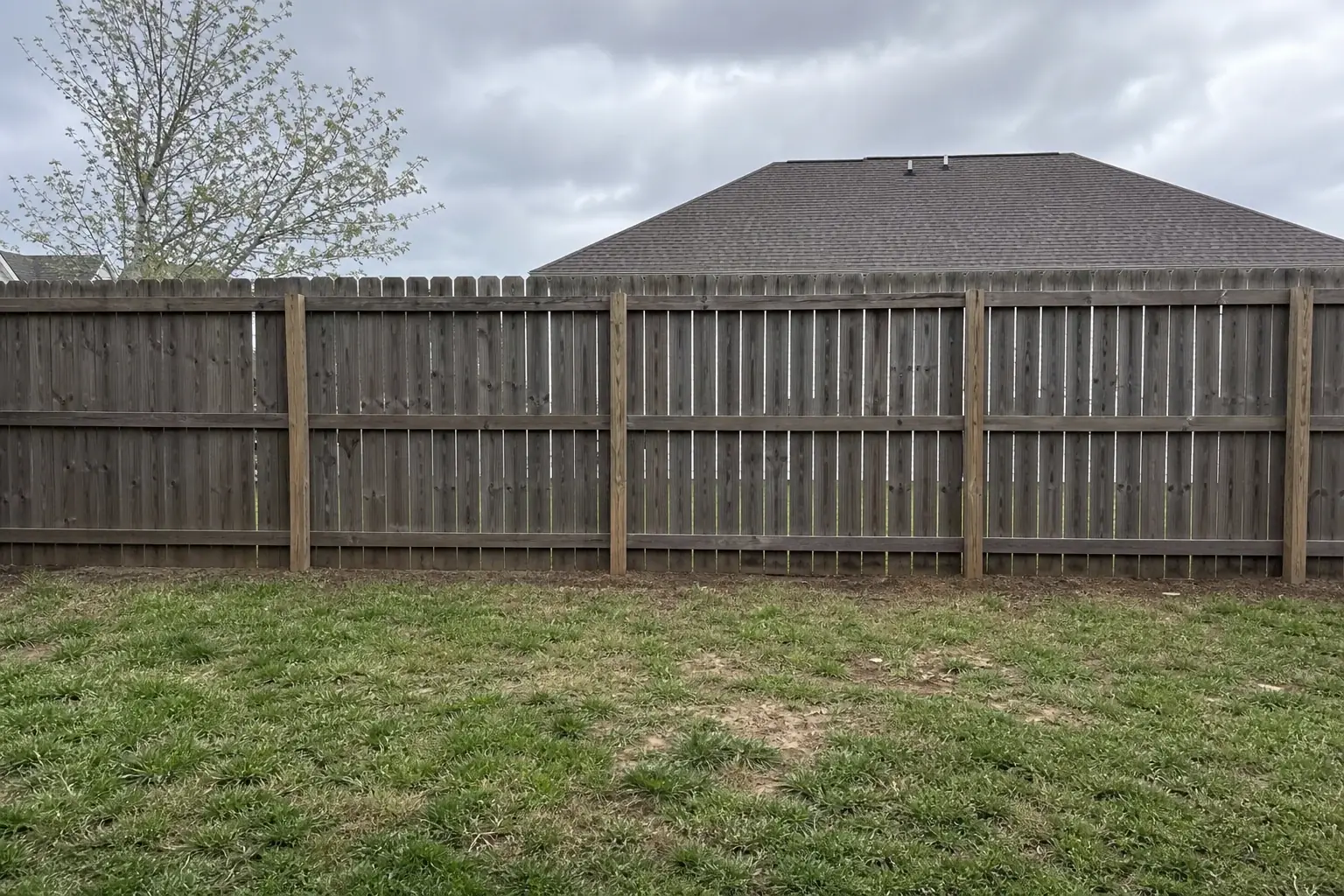 Open residential backyard fence line with no plantings and neighbor's yard visible through gaps