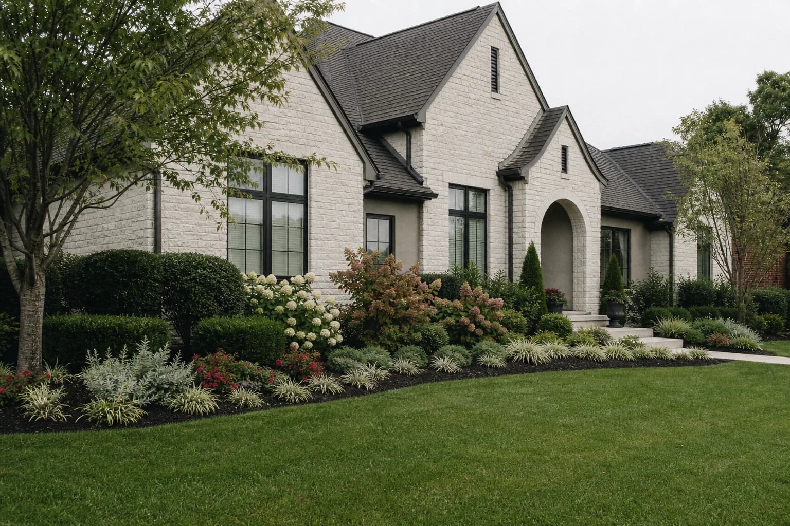 Layered foundation planting with evergreen shrubs, flowering hydrangeas, and low plants along a Lexington home