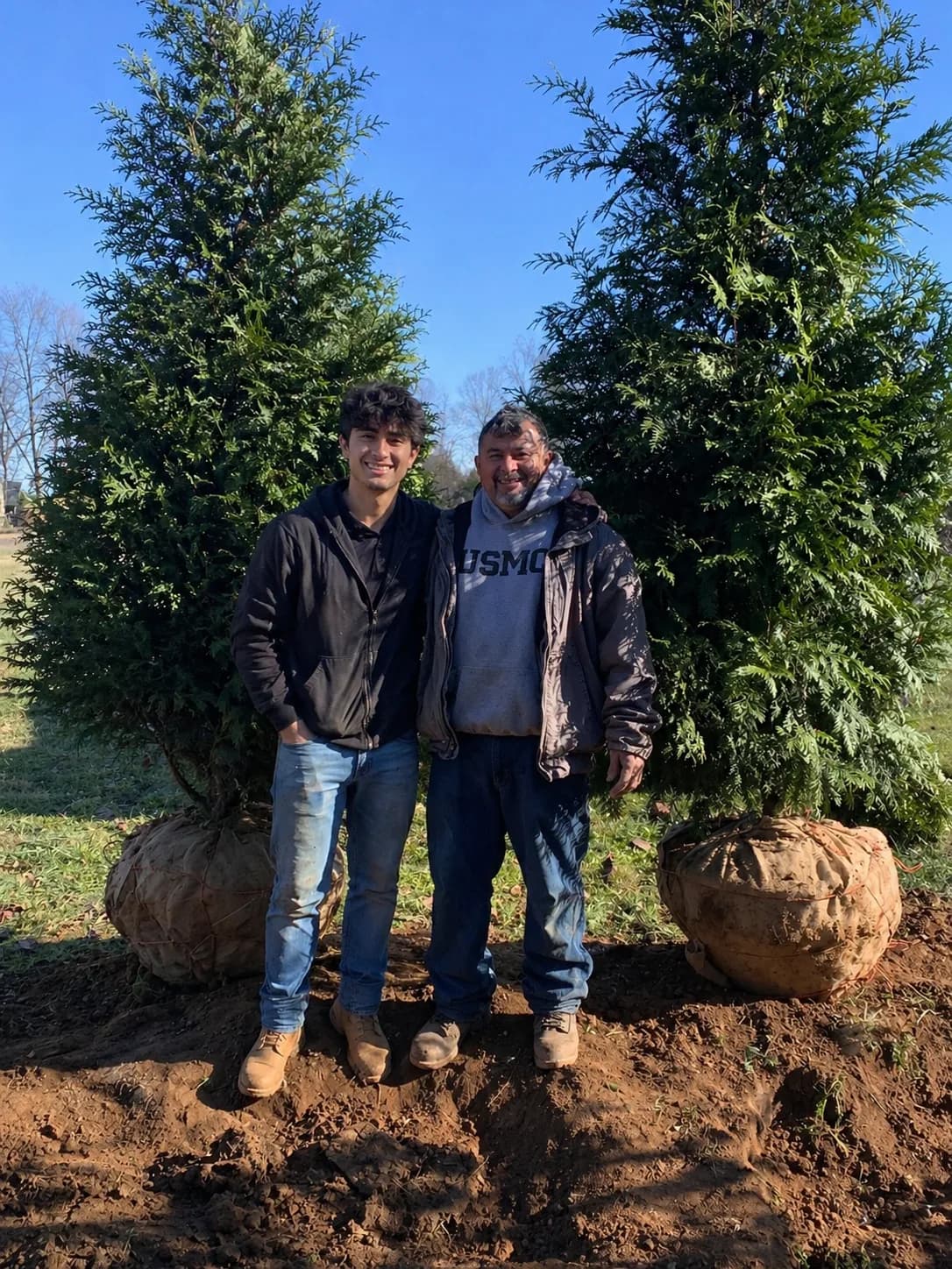 Orlando's Landscaping family team standing with arborvitae trees ready for planting