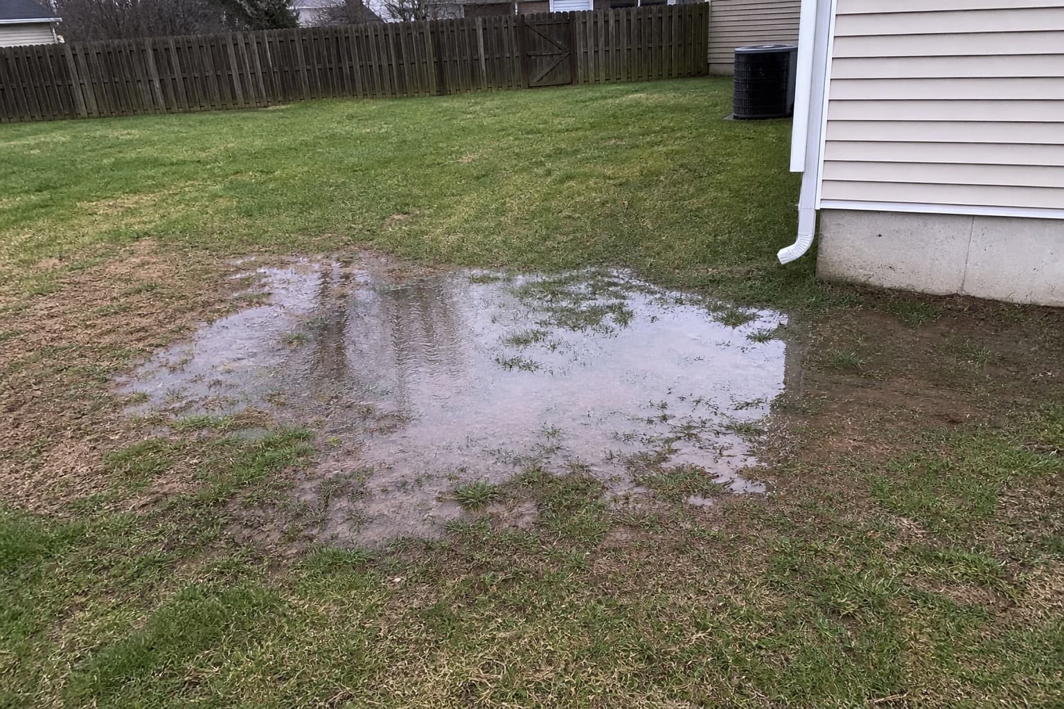Backyard lawn with standing water and a muddy low spot near a home after rain
