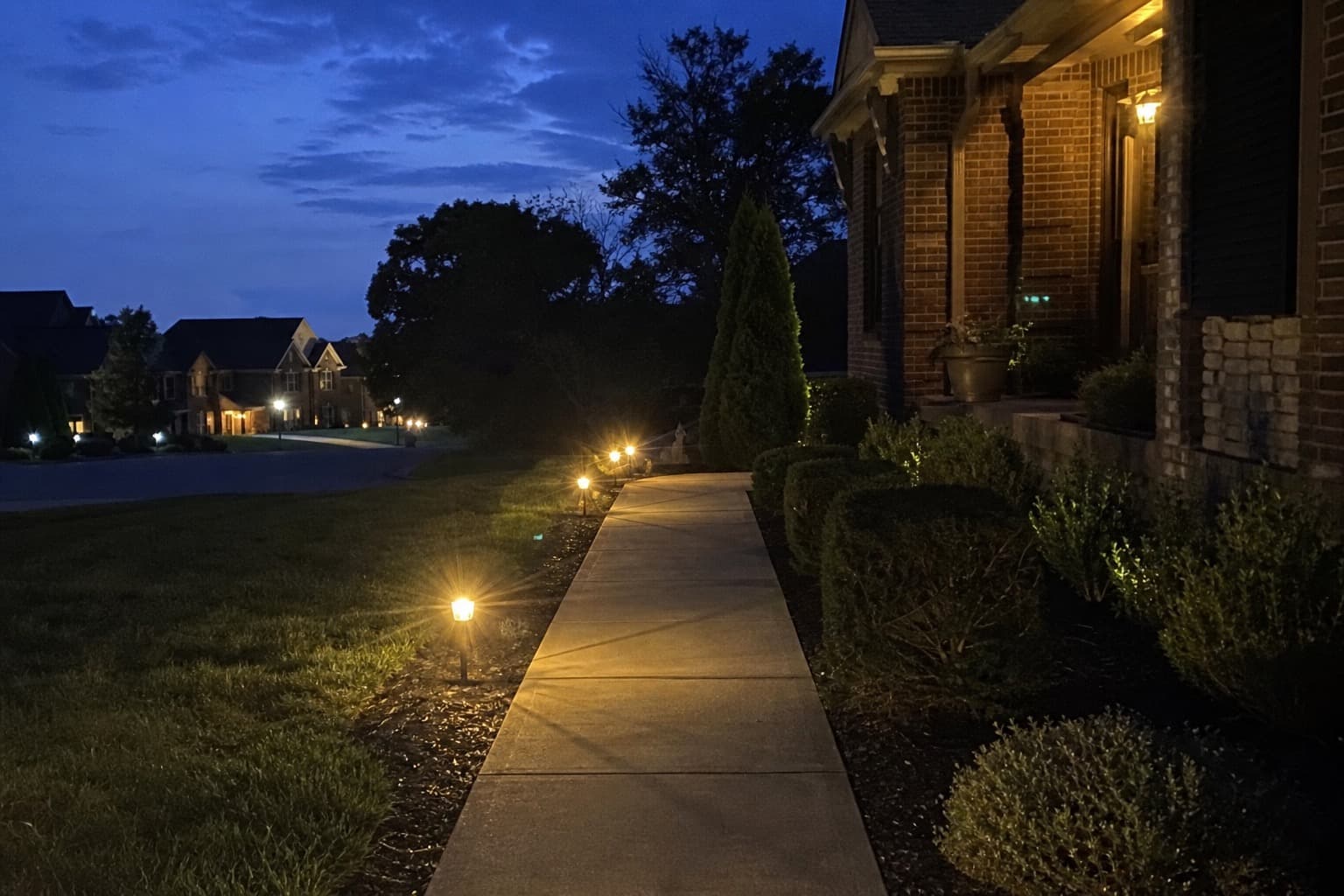 Landscape lighting illuminating a residential home and front walkway at dusk