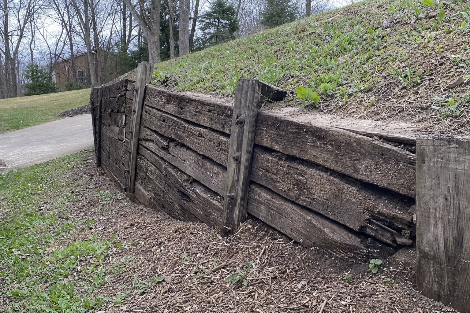 Aging timber tie retaining wall leaning and bowing on a slope