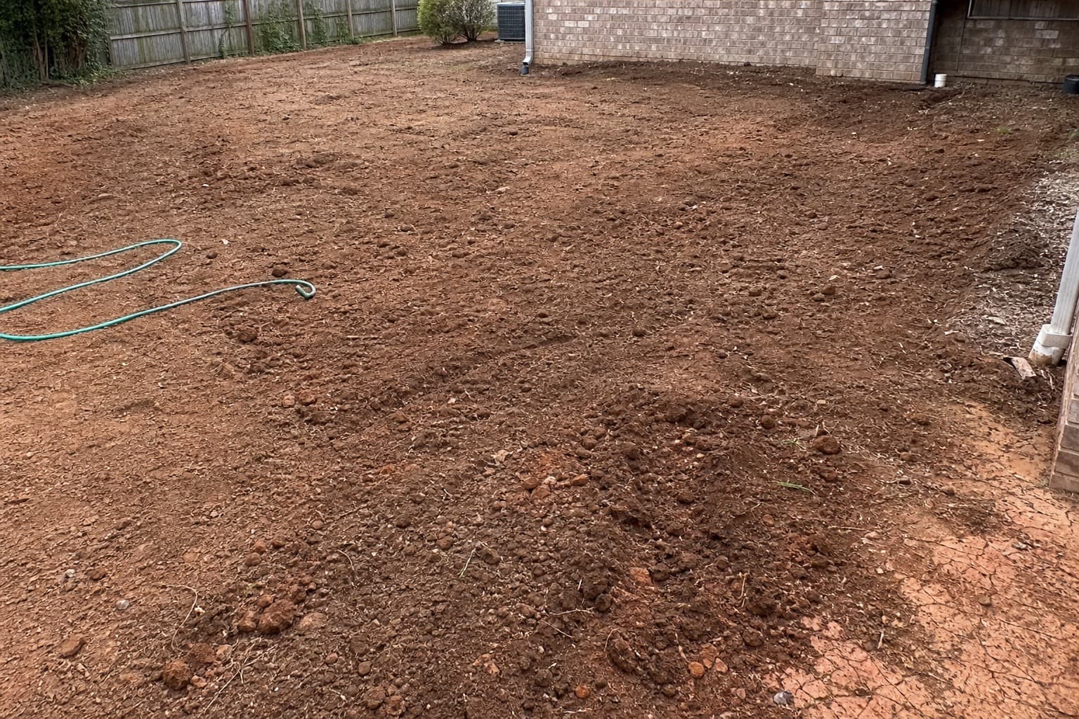 Bare soil lawn area before sod with hose and uneven grade visible
