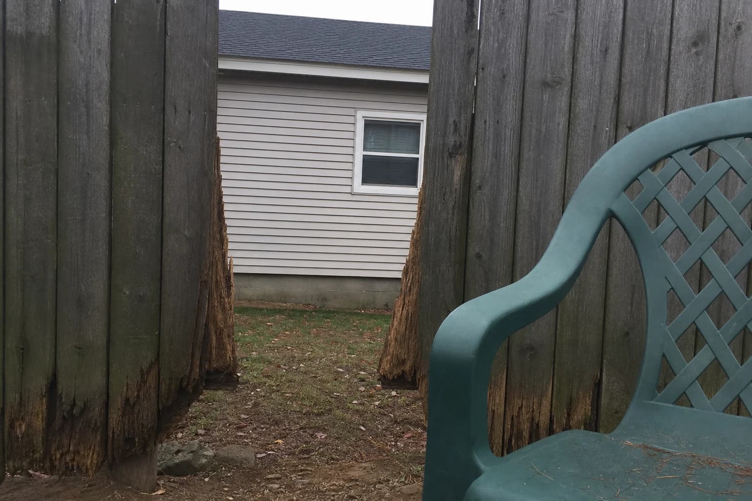 Backyard view looking through a fence gap at a neighbor's house, showing a need for privacy