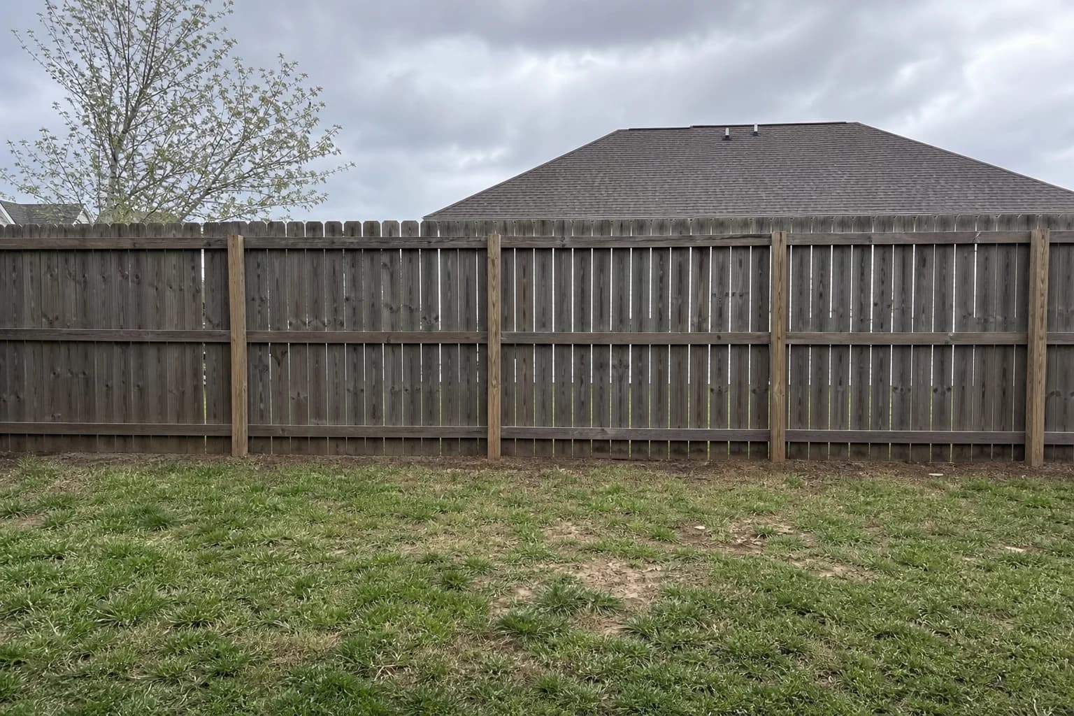 Open residential backyard fence line with no plantings and neighbor's yard visible through gaps